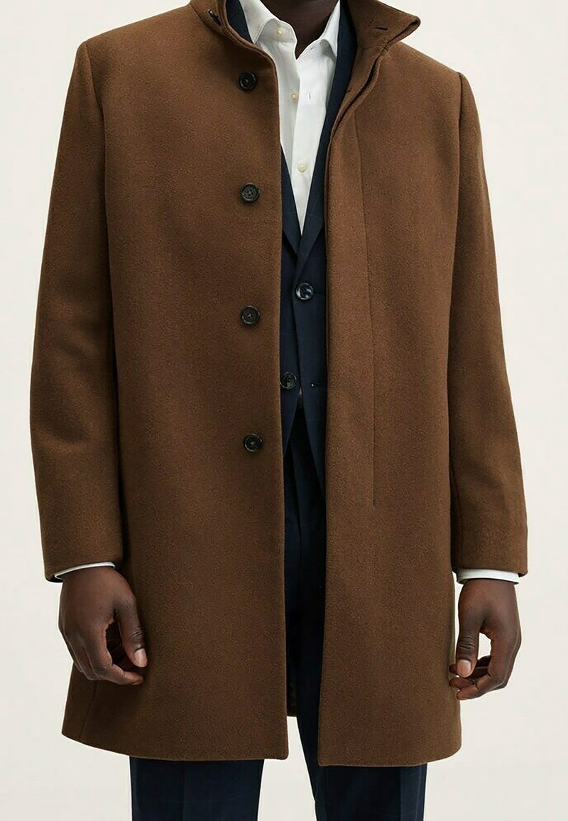 Cappotto in lana marrone con colletto alto, dotato di sei bottoni neri e taglio dritto. Tessuto morbido con un design sartoriale.
