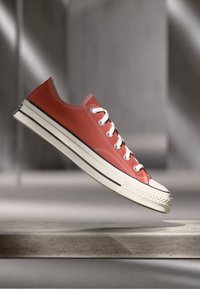 Piros vászon sportcipő fehér fűzőkkel, fekete gumitalppal és toe cap-pel; a klasszikus, alacsony profilú dizájn kontrasztos elemekkel.