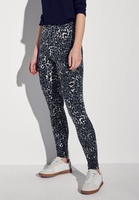 Zwarte en grijze legging met luipaardprint, met een gladde textuur, gecombineerd met witte sneakers met lichtbruine accenten.
