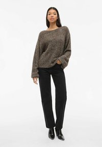 Barna kötött pulóver laza szabással és széles nyakkivágással, fekete, egyenes szárú nadrággal és fekete bokacsizmával párosítva. Puha textúra és kényelmes sziluett.