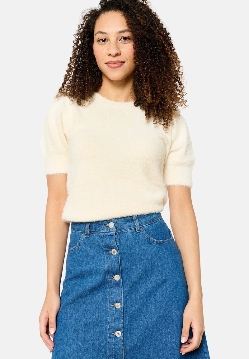 Kremna kratka majica s kratkimi rokavi iz mehkega pletenega materiala, v kombinaciji z denim krilom z gumbnimi detajli in srednjim pasom.