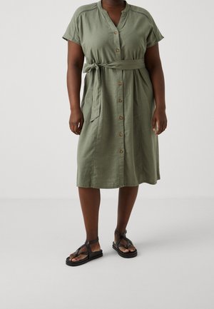 Olive green linen dress with short sleeves, button front, tie waist, and side pockets. Matched with black strappy sandals.