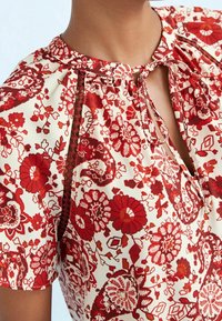 Rood bloempatronen blouse met een ronde halslijn, een sleufsluiting met strik en delicate stitching. Gemaakt van lichtgewicht stof met een zachte textuur.
