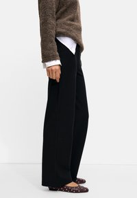 Brown textured sweater layered over a white shirt, paired with high-waisted black wide-leg trousers and burgundy flats with silver studs.