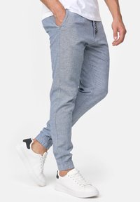 Pantalons de jogging bleu clair en tissu texturé, dotés d'une taille élastique, de poches avant et de poignets ajustés. Portés avec des baskets blanches.