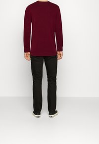 Burgundyröd tröja med långa ärmar och ribbade muddar, kombinerad med svarta slim-fit byxor och avslappnade svarta skor. Minimalistisk design och textur.