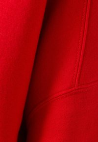 Tissu rouge avec une texture douce et un léger éclat. Présente des coutures visibles et un design lisse et épuré.