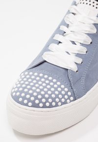 Baskets en daim bleu avec semelle blanche épaisse, lacets en satin blanc et décorations en perles blanches sur le bout renforcé.