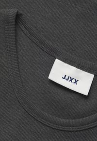 Tamno siva rebrasta majica s okruglim izrezom. Oznaka na ovratniku prikazuje "JJXX" u plavoj boji na bijeloj pozadini.