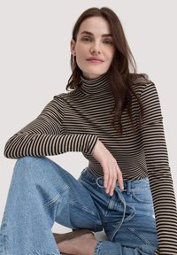 Gestreifter Rollkragenpullover in Dunkelbraun und Beige, aus weichem Stoff. Kombiniert mit hellen, hochtaillierten Jeans im lockeren Schnitt.