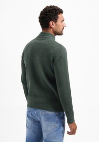 Groene ribgebreide trui met een hoge kraag, aansluitend ontwerp en lange mouwen, gecombineerd met lichtblauwe denim jeans.