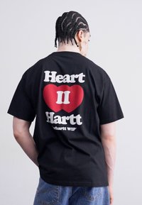 Zwarte katoenen t-shirt met opvallende witte en rode grafische tekst op de achterkant, met een hartontwerp en de slogan "Heart II Hartt".
