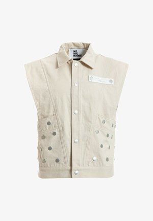 Chaqueta sin mangas beige con botones de presión en la parte delantera, dos bolsillos laterales con tachuelas metálicas, cuello ancho y etiqueta que dice "MOD WAVE MOVEMENT."