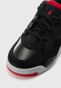 Baskets noires en cuir lisse et daim, avec des accents rouges, des lacets texturés et une semelle en caoutchouc avec un intercalaires gris.