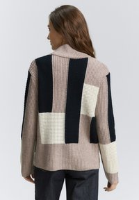 Cardigan en tricot beige, marine et blanc avec un design en patchwork. Présente une texture côtelée et un col rabattu. Met en valeur une coupe décontractée.