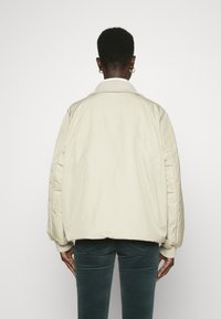 Beige quiltet bomberjakke med ribbet krave, oversized pasform og sidelommer. Glat tekstur og elastiske manchetter.