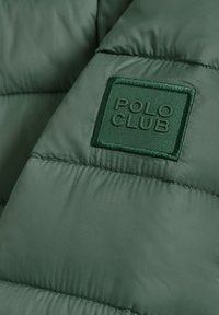 Zelená péřová bunda s prošívaným vzorem a texturovanou látkou. Na boku je výrazně umístěna čtvercová nášivka s nápisem "POLO CLUB" ve stejné zelené barvě.