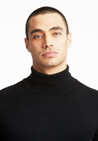 Črna turtleneck pulover iz rebraste pletenine, z visokim ovratnikom in prilagojeno zasnovo, ki ponuja gladko teksturo in čiste linije.