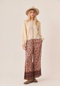 Top de manga larga color crema con tejido texturizado y detalles de encaje, acompañado de pantalones de pierna ancha con un estampado floral y ribete decorativo.