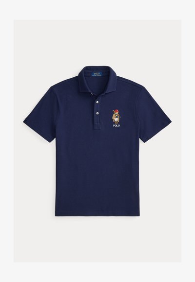 Polo bleu marine avec une patte de boutonnage à trois boutons, manches courtes, et un logo brodé représentant un personnage portant un chapeau. Fabriqué en coton.