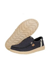 Zapatos cómodos tipo slip-on con un upper textil oscuro, suela de goma beige y un patrón texturizado en la suela. Costuras decorativas y detalle del logo.