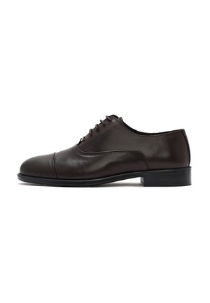 Zapato Oxford de cuero negro con cordones cerrados, puntera con tapa, tacón bajo y acabado pulido liso sobre fondo blanco.