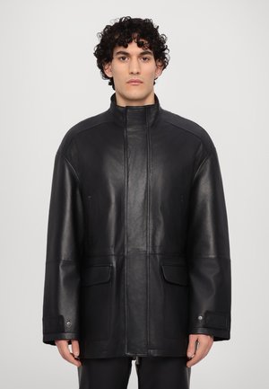 Veste en cuir noir avec un col haut, deux poches avant et une coupe ample. Texture lisse avec des détails de couture minimaux.