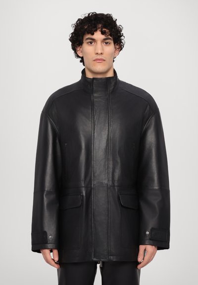 Zwarte leren jas met een hoge kraag, twee voorzakken en een losse pasvorm. Gladde textuur met minimale stikseldetails.