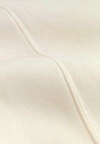 Beige fabric with a smooth texture, featuring subtle raised stitching patterns and a consistent, light color throughout.