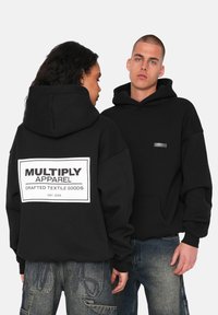 Musta huppari, joka on valmistettu pehmeästä kankaasta, sisältä�ä suuren painatuksen selässä, jossa lukee "MULTIPLY APPAREL", sekä pienen tarran etuosan vasemmalla puolella.