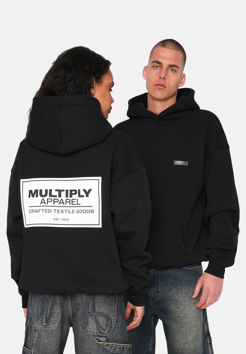 Musta huppari, joka on valmistettu pehmeästä kankaasta, sisältää suuren painatuksen selässä, jossa lukee "MULTIPLY APPAREL", sekä pienen tarran etuosan vasemmalla puolella.