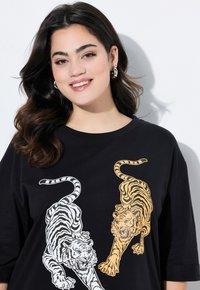 Camiseta negra con gráficos de tigre blancos y naranjas en la parte frontal. La camiseta tiene un cuello redondo y mangas de tres cuartos.