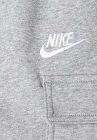 Szürke szövet, melírozott textúrával, a jobb felső részen egy hímzett fehér Nike logóval és egy varrott zsebdísszel.