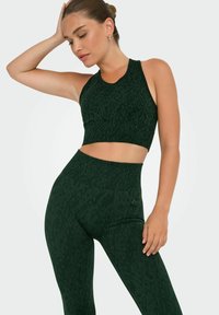 Sostegno sportivo verde scuro e leggings a vita alta con un sottile motivo leopardato. Tessuto testurizzato, design aderente e costruzione senza cuciture.