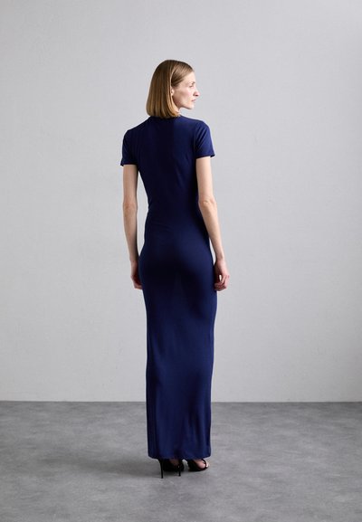 Sötétkék, testhez simuló maxiruha rövid ujjakkal. Sima szövettextúra, bokáig érő kialakítás, fekete magassarkú cipővel párosítva.