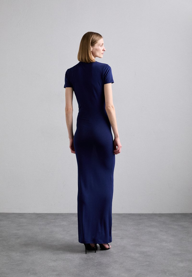 Navy blue, form-fitting maxi dress with short sleeves. Smooth fabric texture, ankle-length design, paired with black high heels.