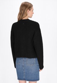 Maglione nero a maglia con design cropped, texture a coste e collo a giro, abbinato a una mini gonna in denim blu.