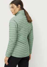 Chaqueta acolchada en verde apagado, con un alto cuello y un patrón de acolchado en forma de chevrón. Textura suave con mangas y dobladillo ajustados.