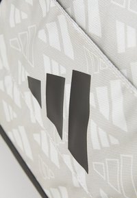 Bolsa de tela gris con un patrón texturizado, que presenta acentos negros llamativos y diseños geométricos. La vista en primer plano enfatiza el material y las formas.