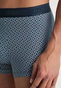 Marineblauwe boxershorts met een patroon van golvende lijnen en cirkels, voorzien van een gemarmerde elastische tailleband met de merknaam.