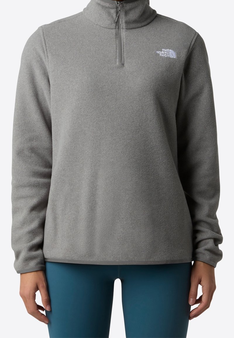 Personne portant un pull polaire gris à fermeture éclair quart avec le logo The North Face sur la poitrine et un legging bleu sarcelle, visible du cou jusqu’aux hanches.