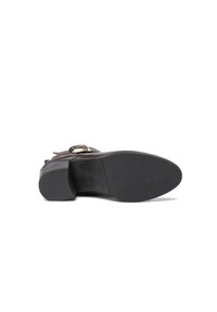 Bota de cuero marrón con una textura suave, que presenta una suela de goma negra y acentos de metal cerca de la correa del tobillo.