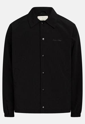 Veste noire avec fermeture boutonnée à l'avant, col pointu et poignets élastiques. Comprend des poches latérales et un logo brodé discret.