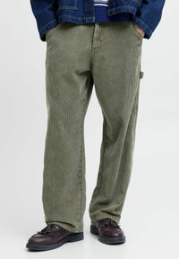 Grønne cordbukser med rett ben, med vertikale striper og en sidelomme, kombinert med mørke sko.