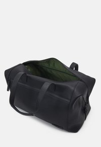 Sac de sport en cuir noir avec un intérieur spacieux de couleur verte, des poignées de transport doubles et une fermeture éclair. Surface texturée avec des détails subtils.