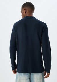 Marinblå långärmad skjorta med texturerad tyg, en enkel design och en avslappnad passform, kombinerad med ljusa denimshorts.