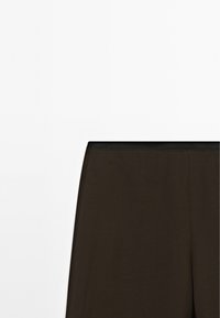 Hnědé legíny s jednoduchým designem, vyrobené z měkkého materiálu, s černým elastickým pasem. Textura se zdá být hladká a elastická.