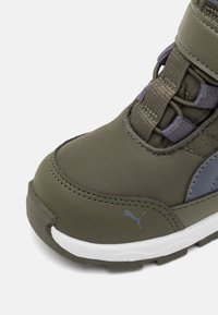 Baskets de sport en nylon vert avec une finition texturée, présentant un accent gris et des lacets élastiques. Semelle en caoutchouc avec un motif de bande de roulement bien marqué.