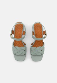 Sandales bleu clair avec un design tressé, dotées d'un bout carré et d'une sangle de cheville. La semelle intérieure texturée en tan ajoute un contraste et une adhérence.