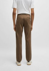 Bruine rechte broek gemaakt van zacht materiaal, voorzien van twee achterzakken en een klassieke tailleband, gestyled met witte sneakers.